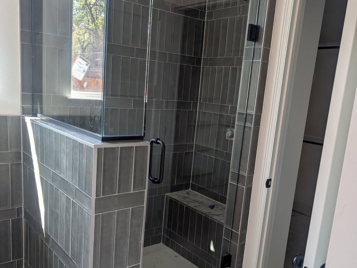 Tiled walk-in shower with a built-in bench and a custom glass door with a black handle, installed by Bob's Shower Plus