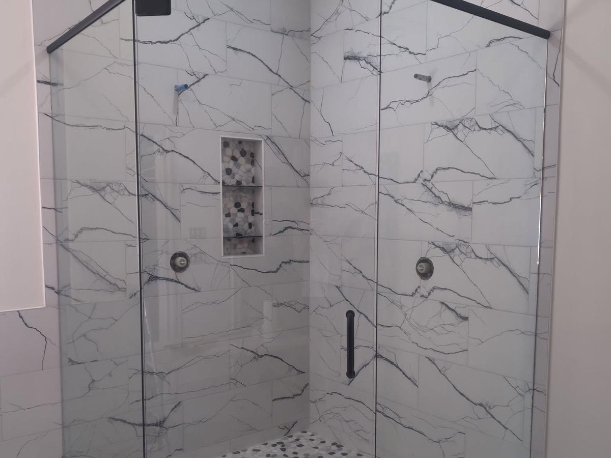 Marble-look corner shower with clear glass panels and a black header bar, installed by Bob's Shower Plus