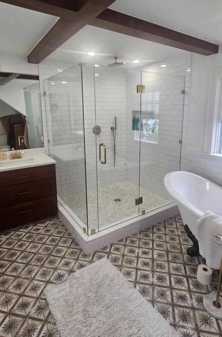 Frameless glass corner shower enclosure with brass-tone hinges, clamps and handle next to a clawfoot tub, installed by Bob's Shower Plus
